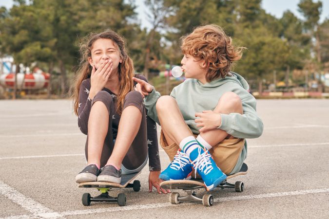 Positive teen skaters blowing bubble gum in city