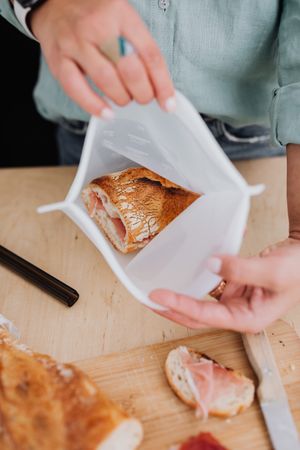 Cropped image of a man holding a plastic bag with ham sandwich in it