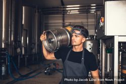 Young white male wearing apron and goggles on head in keg storage room 0yljab