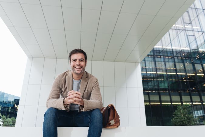 Cheerful manager sitting outside modern building