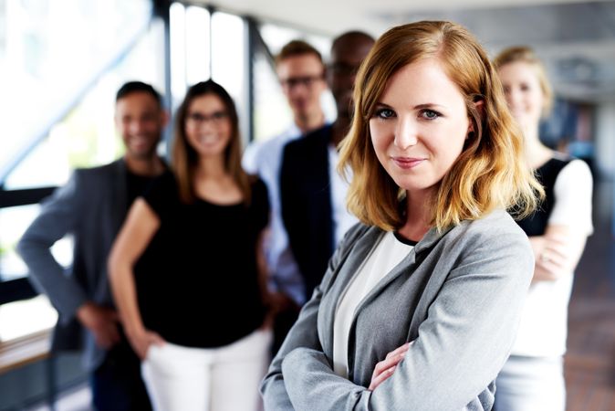 Business woman smiling with her arms crossed in front of colleagues at work