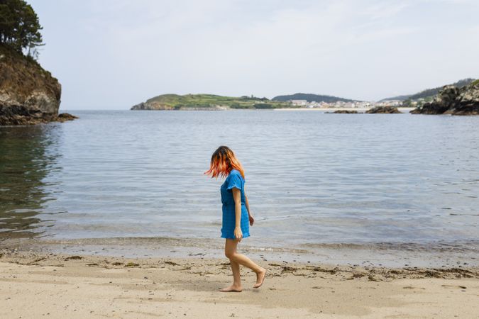 A young woman with orange hair strolls calmly along the seashore on a natural beach in northern Galicia