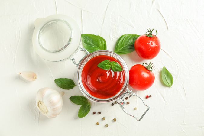 Flat lay composition with fresh tomatoes, basil, pepper, garlic and sauce in glass jar on blank background, space for text and top view