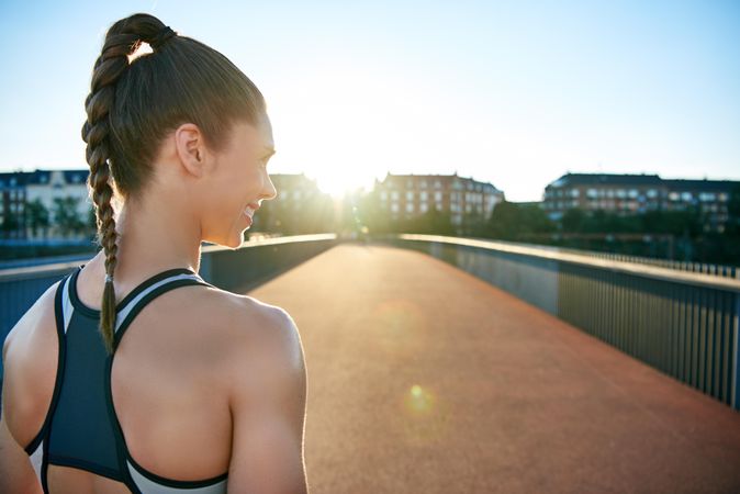 Back of smiling athletic woman on sunny bridge
