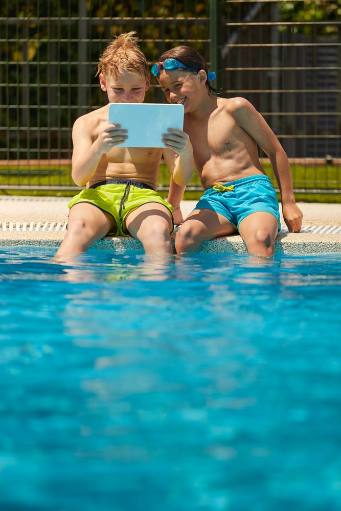 Boys on poolside browsing tablet