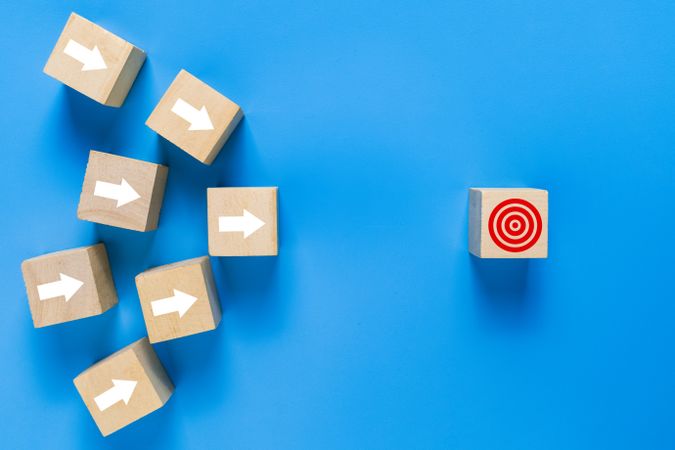 wooden blocks with arrow pointing on target isolated on blue background. concept of goals achievement