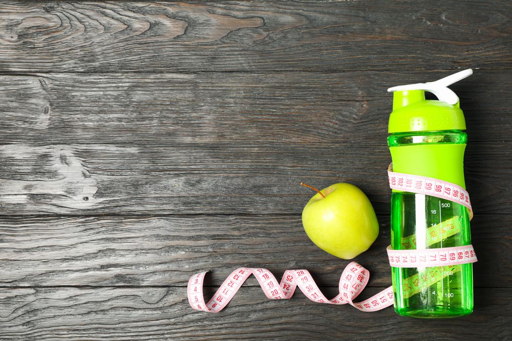 Bottle, measuring tape and apple on wooden background, copy space