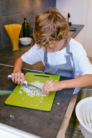Focused boy cutting fresh onion while cooking in kitchen