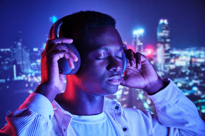 Black man in headphones listening to music against night city