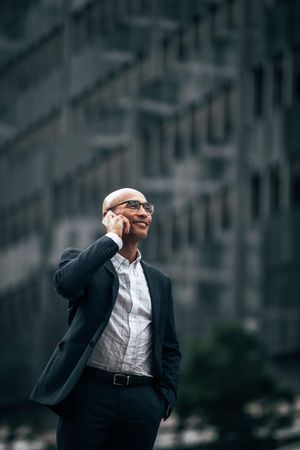 Smiling businessman talking over cell phone standing outdoors with a hand in pocket