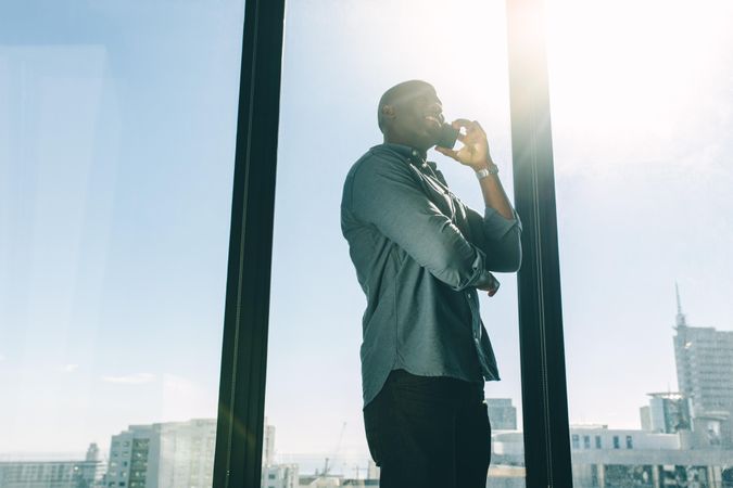 Businessman talking on cellphone in modern office with city view and sunlight