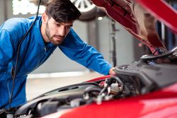 White man working on engine auto repair shop on red car