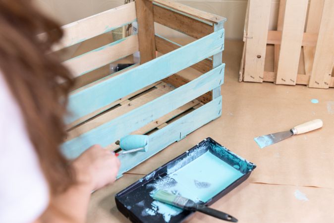 Woman paining wooden box in blue color with roller