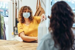 Clothing store owner wearing protective face mask giving a shopping bag to female customer