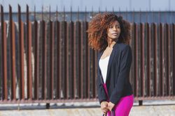 Black female standing in front of brown wall in the sunshine while looking away