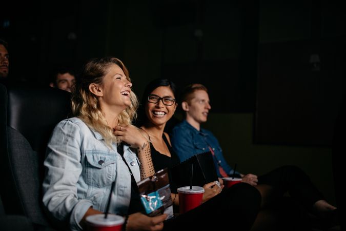 Friends sitting in movie theater with popcorn and drinks