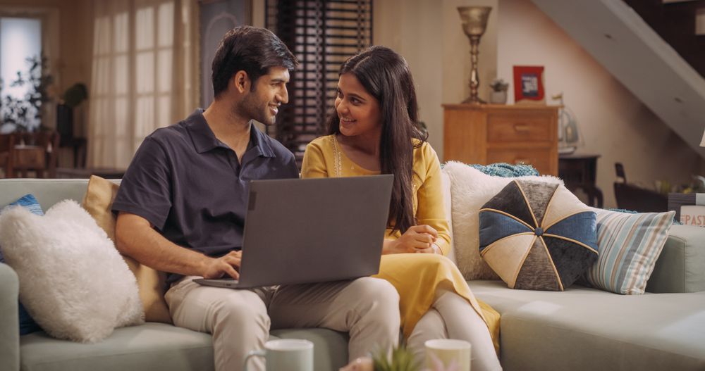 Portrait of Loving Young Indian Couple Enjoys Browsing Online Shopping Websites Together On A Laptop