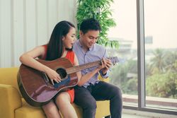 Man and woman having fun playing guitar on yellow couch