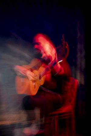 Hispanic man playing acoustic guitar during flamenco performance on dark stage