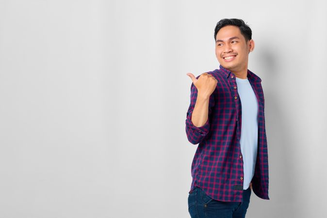 Asian male in grey studio with pointing thumb to the side