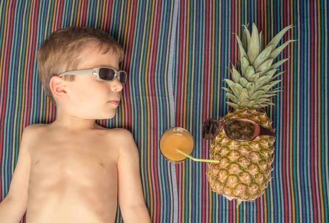 Happy child and pineapple sunbathing over a towel