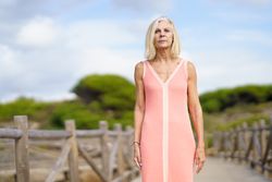 Older woman with grey hair standing on wooden walkway near the coast, copy space