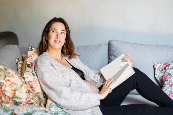 Relaxed pregnant woman reading a book on sofa