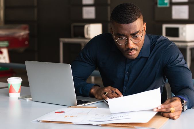 Black man writing in notepad near laptop in office