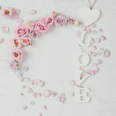Wreath of rose flowers and petals on light background with the word “Love”