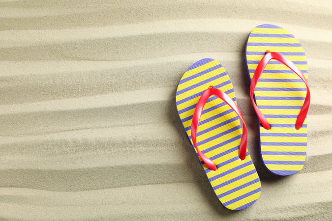Clear sea sand with flip flops, space for text and top view. Summer vacation background