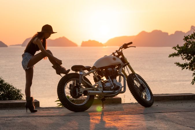 Woman tying boots near motorcycle