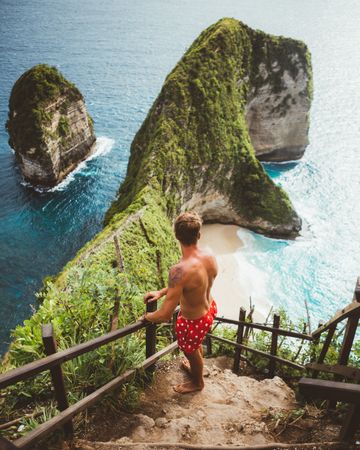 Man on viewpoint above tropical seashore with cliffs