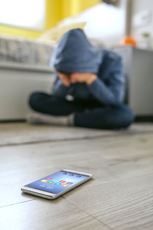 Teenager boy crying desperate for bullying with cell phone lying on the floor in foreground