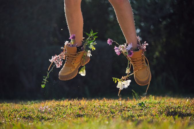 Crop person in boots with flowers jumping in nature