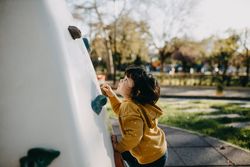 Young girl climbing small rock climbing wall in a park