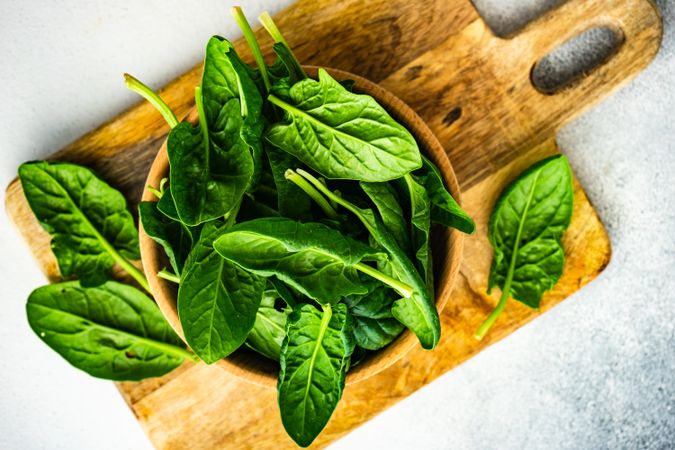 Top view of wooden bowl of fresh spinach on kitchen counter with copy space