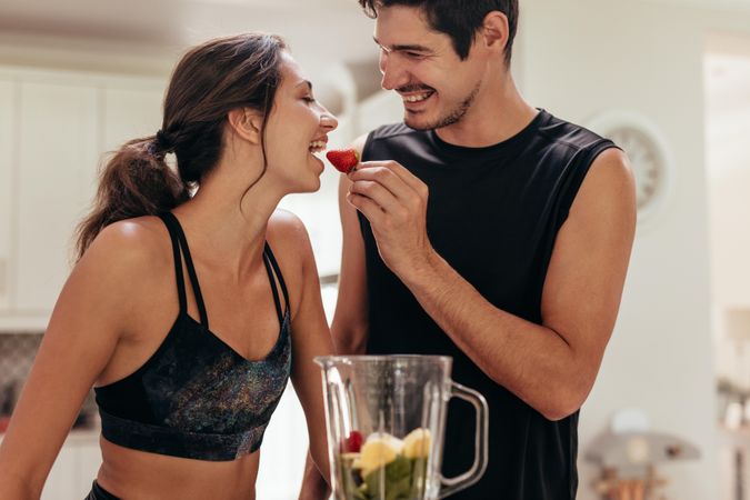 Young man feeding a strawberry to woman in kitchen
