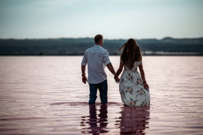 back view of adorable couple walking into an amazing beach with pink water