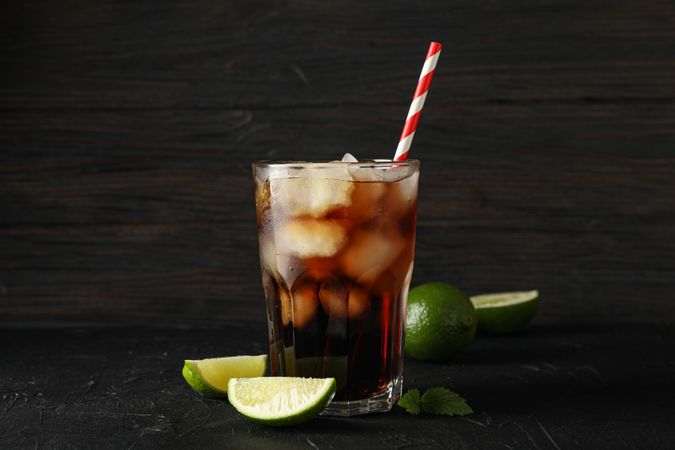 Glass of cold cola and limes on cement background