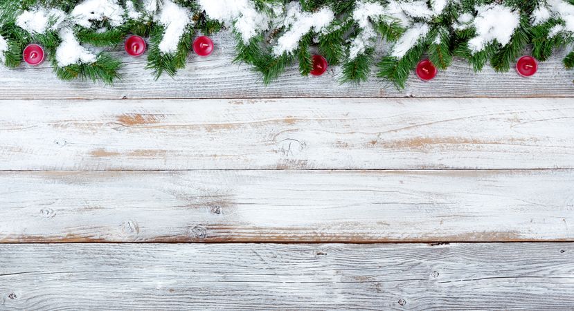 Snowy Christmas evergreen branches and red candles on vintage wooden planks