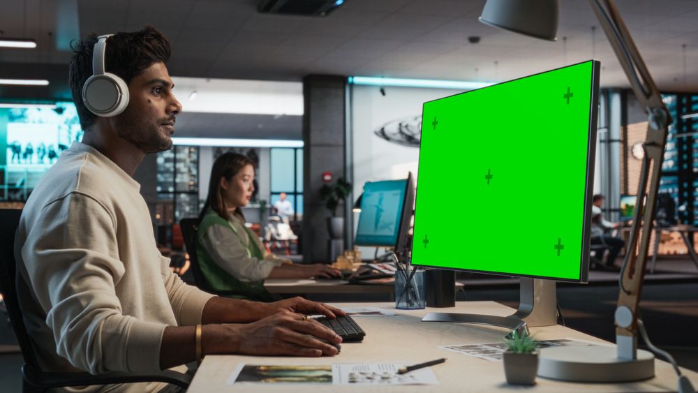 Indian Male Game Designer Using Desktop Computer With Green Screen Chromakey on Display