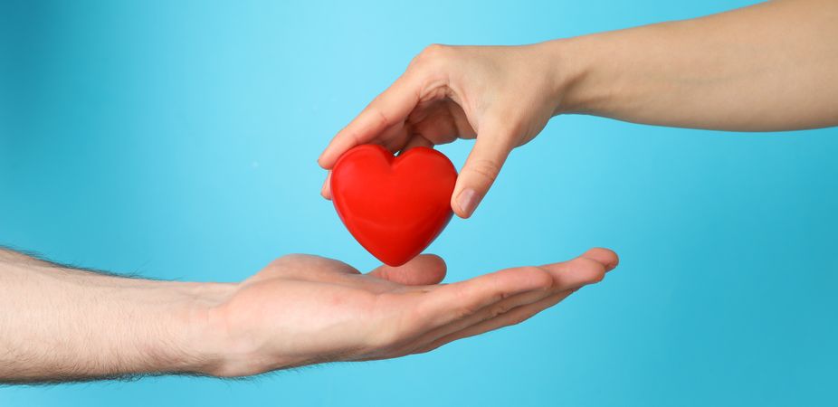 Female hand puts heart on male hand on blue background