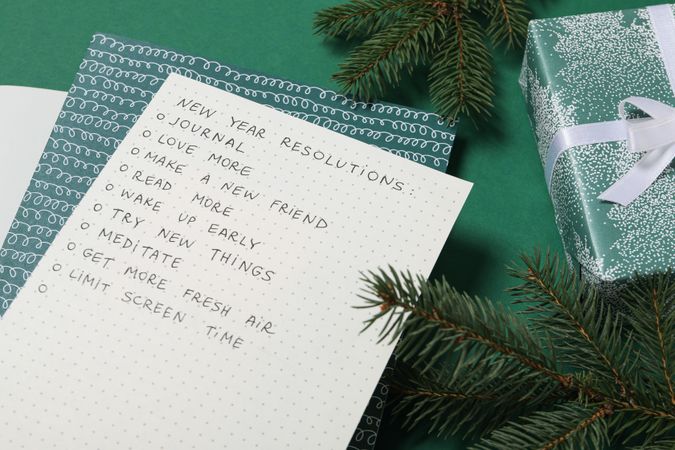 Paper with list, gift boxes and fir branches on green background, close up