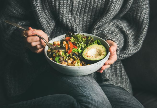 Woman in jeans and sweater eating fresh salad