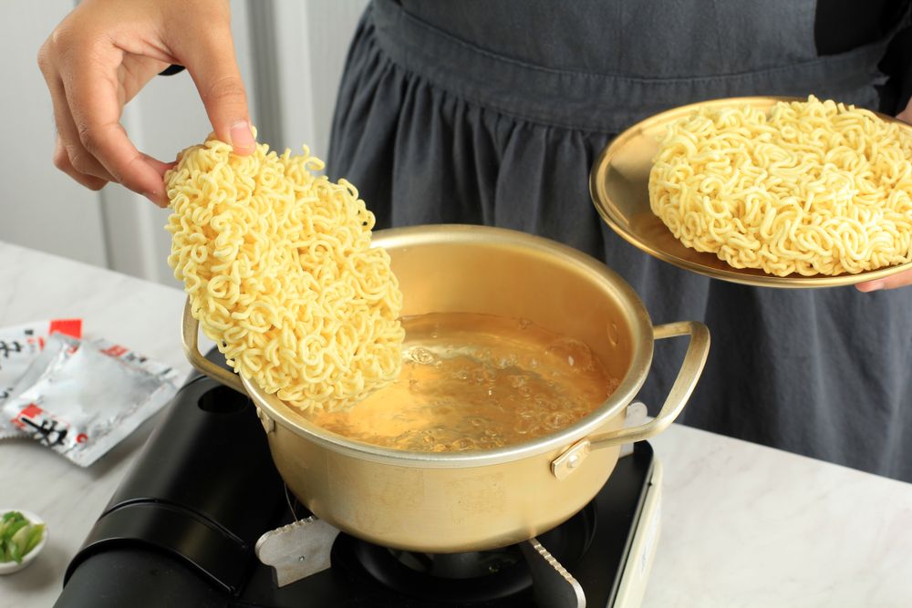 Chef putting circle of dried noodles into boiling water