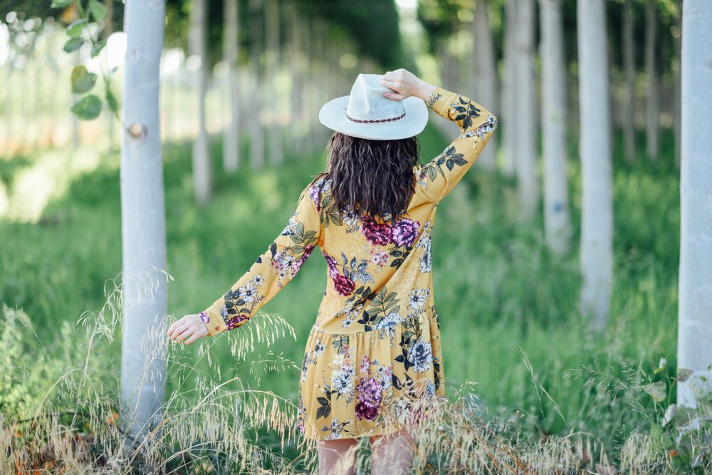 Back of brunette woman in yellow dress and straw hat in green field