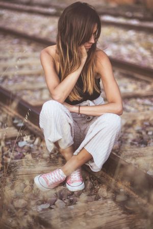 Long haired woman sitting on railways overgrown with dry grass