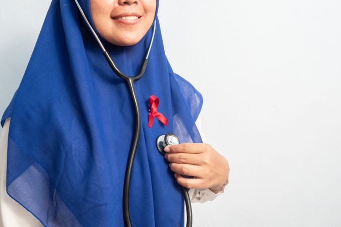 Happy Muslim Female Asian doctor or nurse with Red ribbons and stethoscope, HIV awareness concept, world AIDS day, world cancer day.