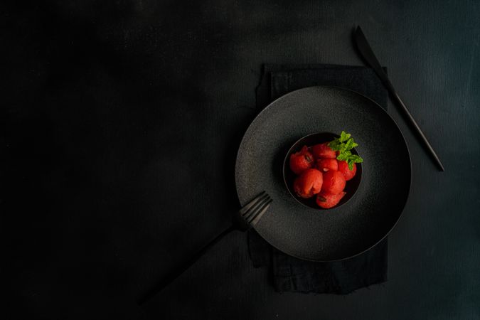 Red sorbet on dark plate, served with napkin and silverware