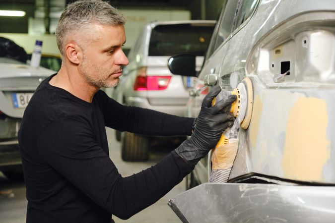 Mechanic grinding paint from car detail